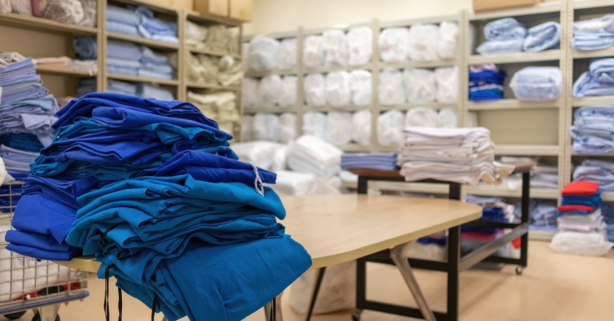 A laundry room in a hospital with shelves stacked with folded clean linens and organized supplies visible.