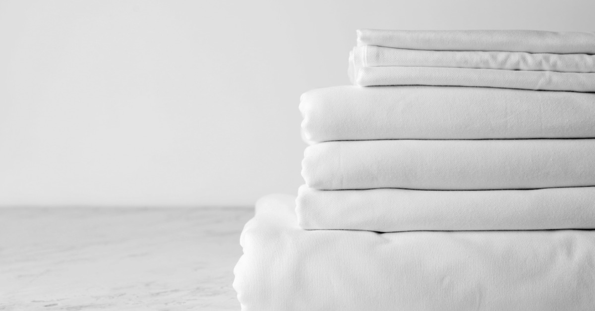 A folded stack of clean, white sheets in different sizes placed on a white surface against a white background.