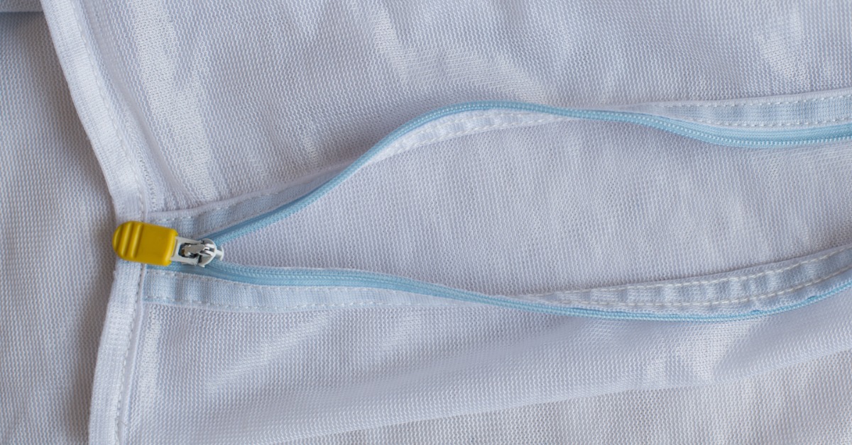 A close-up on an unzipped mesh laundry bag with white mesh, a light blue track, and a yellow rubber zipper.