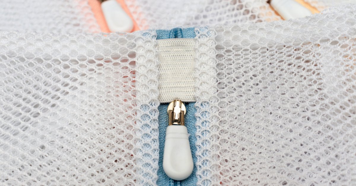 A close-up view of a white mesh laundry bag with a zipper, stacked on top of other bags of the same type.