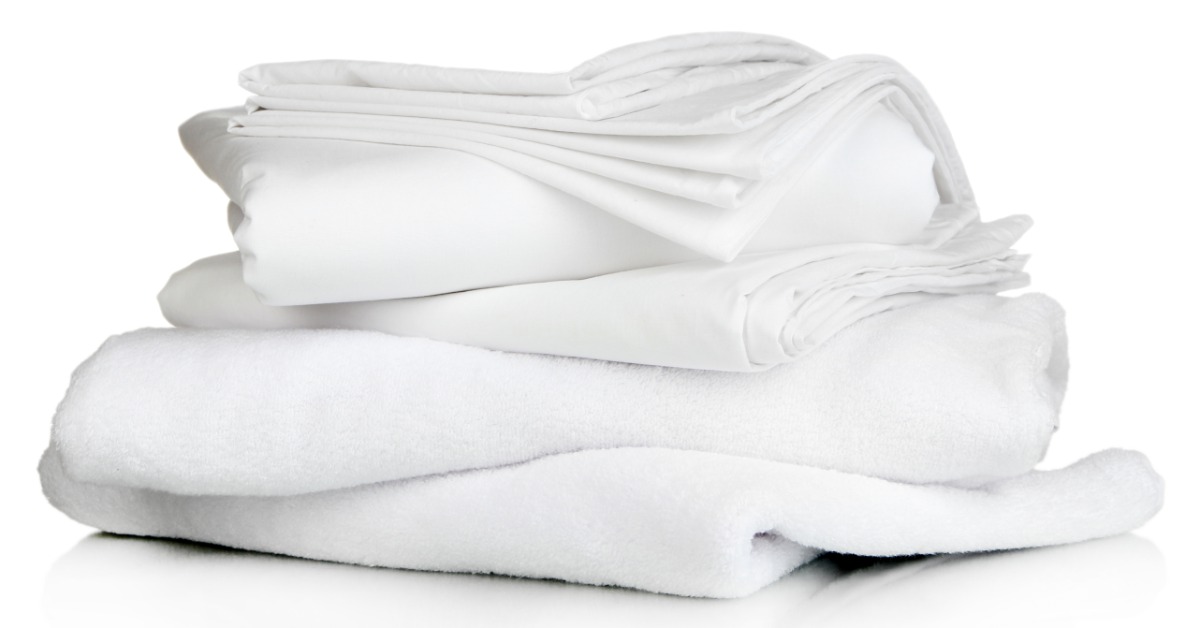 A stack of white folded sheets and plush towels arranged neatly on a clean white surface, with soft layers visible.