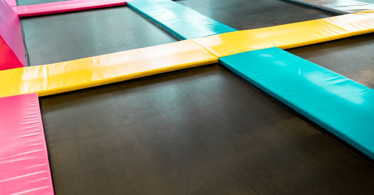 A large indoor trampoline park with interconnected jumping surfaces and padded borders arranged across the floor.