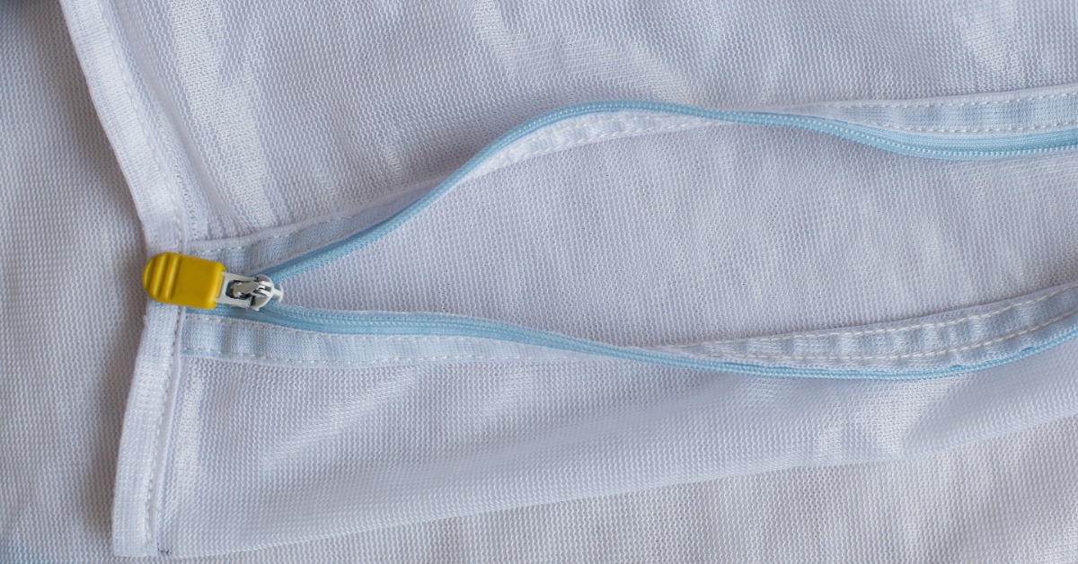 A close-up of white mesh laundry bags overlapping with blue zippers and a small yellow zipper pull visible.