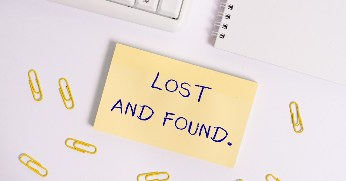 A post-it note with 'Lost and Found' written on it next to yellow paperclips, a keyboard, and a notepad on a desk.