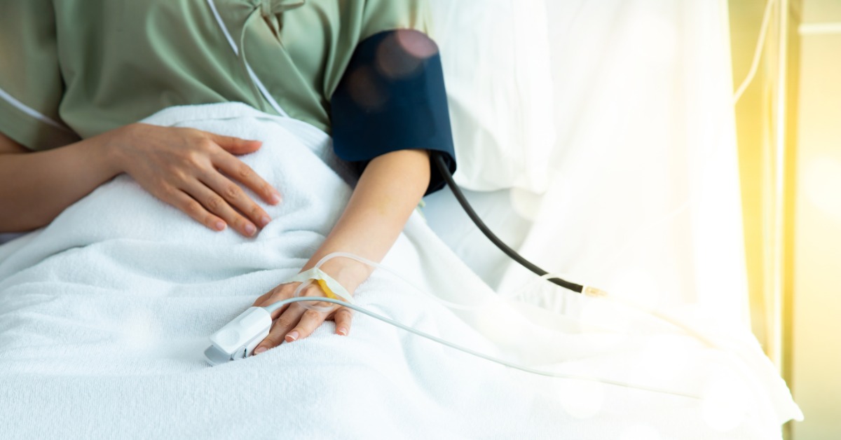 A person lying in a bed with a blood pressure cuff, tubing, and a fingertip sensor attached to one hand.